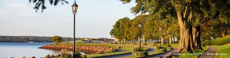 The Charlottetown waterfront: a bike path winds along a river lined with thick trees, benches and tall black lanterns.